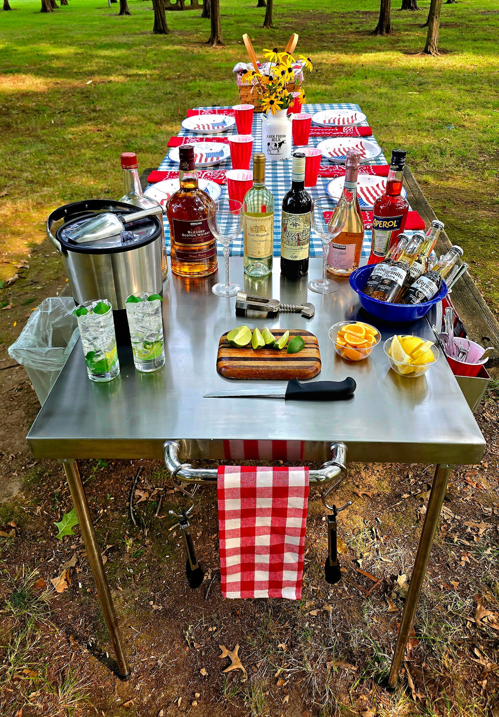 The Big John Table set up as an outdoor drink station with bottles, glasses, ice bucket and cut limes and lemons