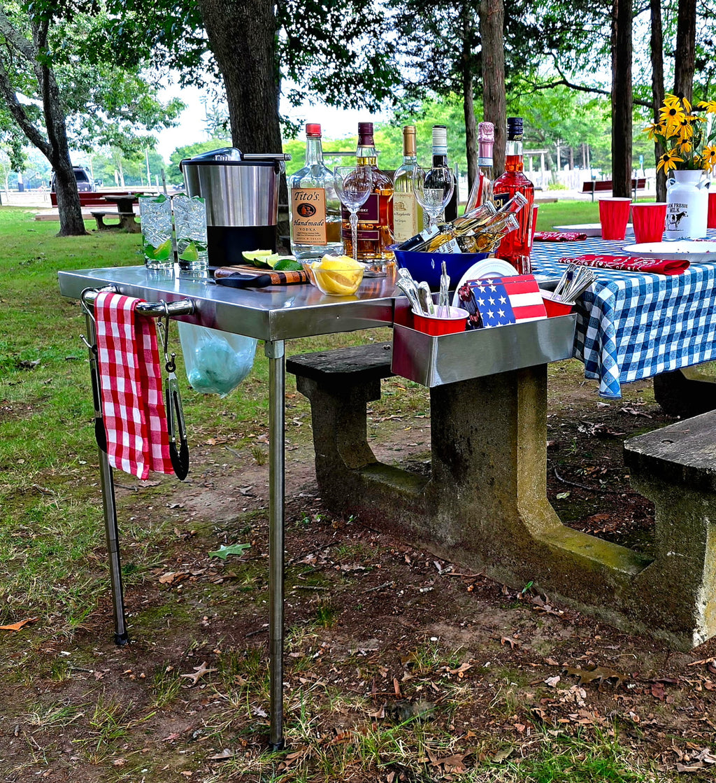 The Big John Table as an outdoor bar with bottles, glasses, an ice bucket, towel bar and utensil caddy
