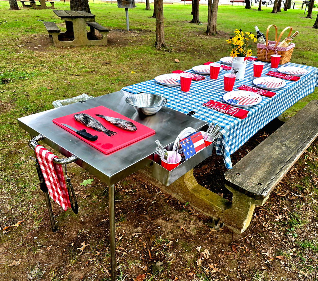 The Big John Table as a food prep station clamped to a picnic table set for a meal in the park