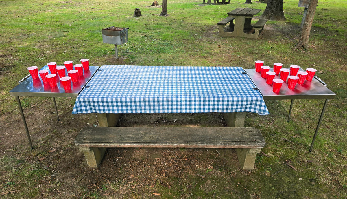 Two Big John Tables clamped to both ends of a picnic table, extending it with stainless-steel surfaces set with red cups